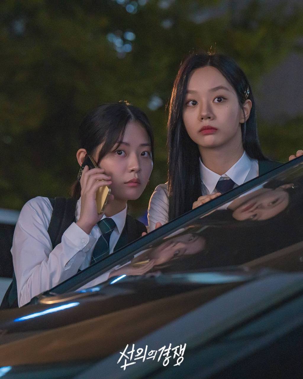 Woo Seul-gi (Chung Su-bin) holding a phone to her ear and Yu Je-i (Lee Hye-ri) looking ahead in shock, both leaning over a dark car bonnet at night in a still from Friendly Rivalry.