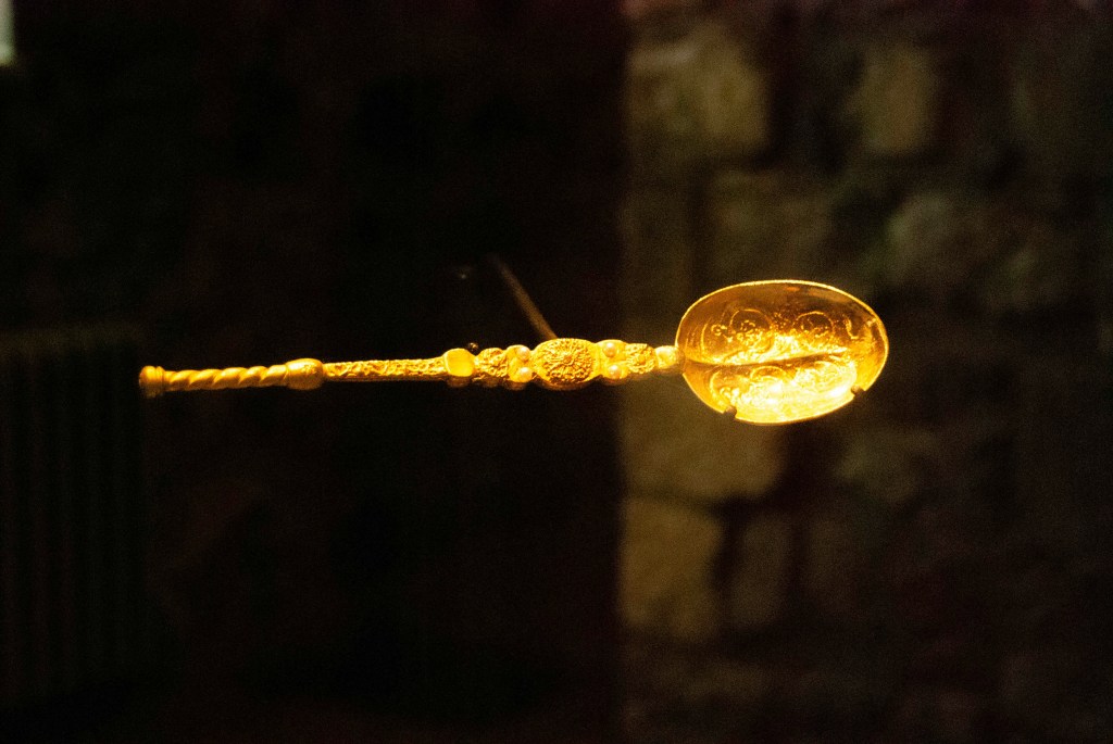 An ornate, glowing golden spoon with intricate patterns set against a dim background.