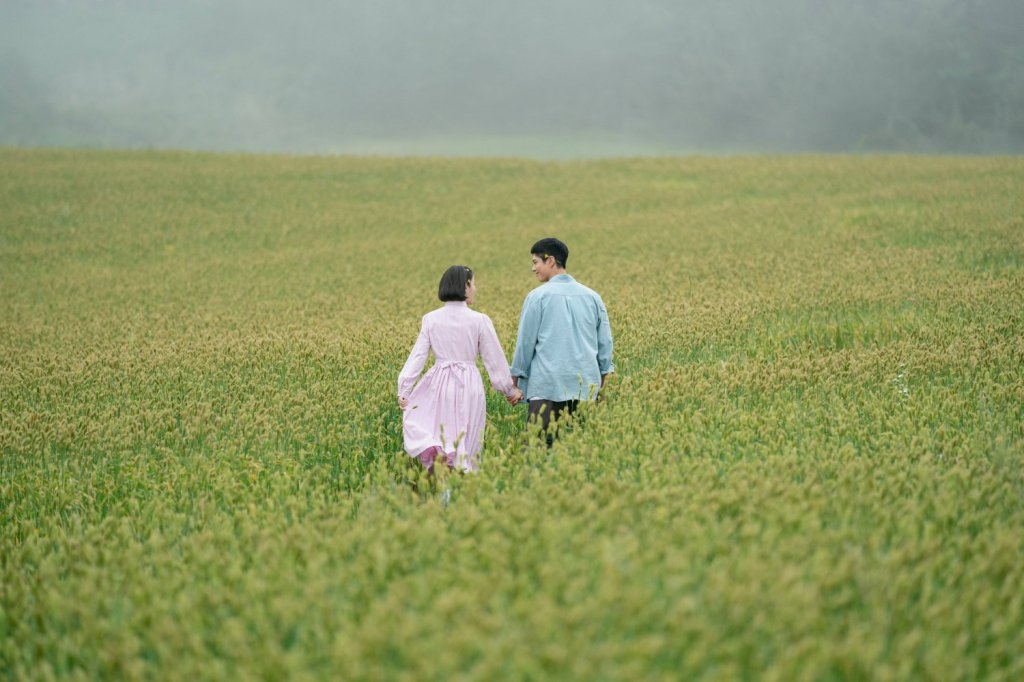 IU (Lee Ji-eun) and Park Bo-gum stand side by side in retro 1950s-style clothing. IU wears a floral top with braids, while Park Bo-gum is dressed in a simple button-down shirt and trousers. Both share gentle, contemplative expressions.